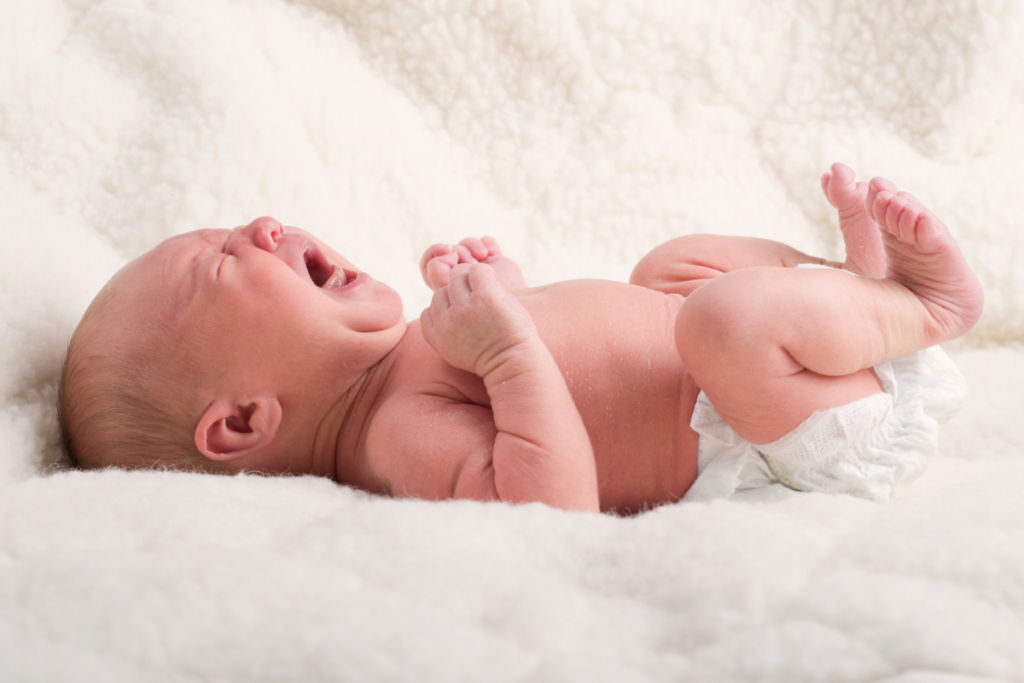 Huilende pasgeboren baby in een luier op een zachte ondergrond.