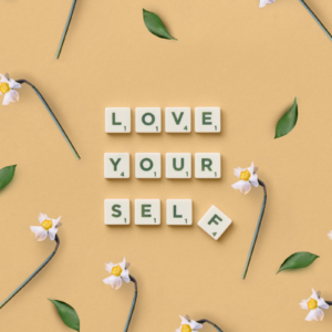 Scrabble letters die de tekst: 'love yourself' vormen op een lichter achtergrond met bloemen